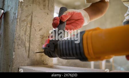 Le maître perce un mur pour fixer le futur bloc de mousse. Un constructeur avec un marteau pneumatique perce un trou dans un mur de béton. Ouvrier masculin démolissant Banque D'Images