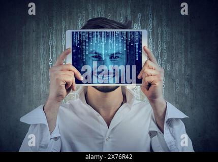 Heureux jeune homme tenant une tablette avec son visage affiché sur un écran avec du code binaire Banque D'Images