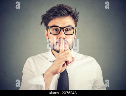 Jeune homme à lunettes hipster du doigt de maintien sur les lèvres pour demander le silence et portrait sur fond gris Banque D'Images