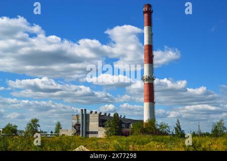 Grande cheminée rayée rouge et blanche d'une chaufferie sur fond de nuages blancs dans le ciel bleu Banque D'Images