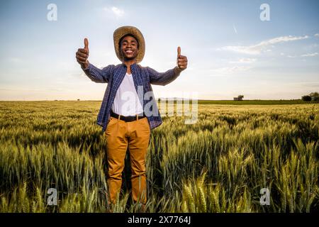 Un agriculteur africain se tient debout dans son champ de blé en pleine croissance. Il est satisfait du progrès des plantes. Banque D'Images