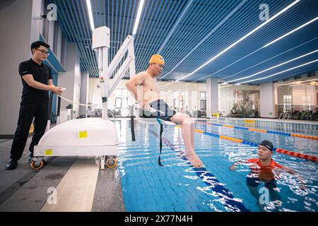 (240518) -- HANGZHOU, 18 mai 2024 (Xinhua) -- Un membre du personnel (l) utilise un ascenseur pour aider un homme handicapé à entrer dans la piscine sans obstacle du centre culturel et sportif de Hezhuang dans le district de Qiantang à Hangzhou, dans la province du Zhejiang de l'est de la Chine, 16 mai 2024. Une variété d'installations sans obstacles ont été mises en place au gymnase, à la piscine, etc dans le centre culturel et sportif de Hezhuang pour mieux répondre aux besoins spéciaux des personnes handicapées. Au cours des dernières années, la ville de Hangzhou a vigoureusement encouragé la construction d'installations urbaines sans obstacles. En 2023, Hangzhou a terminé le renova Banque D'Images