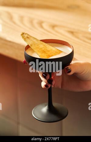 Verre noir de cocktail épicé avec poire caramélisée dans la main féminine Banque D'Images