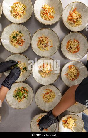 Gros plan sur les mains d'un chef qui prépare des plats avec précision dans une cuisine de restaurant animée Banque D'Images