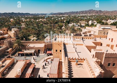 Vue surélevée à grand angle depuis les remparts du fort de Nizwa surplombant la cour intérieure animée, les étals du marché et une vaste oasis de palmiers dattiers à Oman Banque D'Images