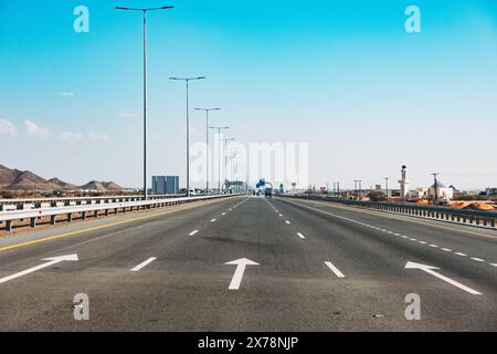 Autoroute moderne et vide à Oman avec des panneaux de limitation de vitesse, des lampadaires et un ciel bleu clair, montrant l'infrastructure routière et les transports Banque D'Images