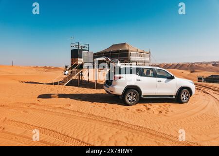 Une Toyota Fortuner blanche stationnée devant une tente sur pilotis à Sharqiya Sands, une région désertique d’Oman remplie de dunes, populaire pour le camping Banque D'Images