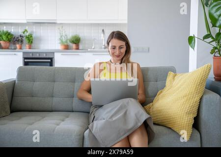 Femme souriante assis sur le canapé à la maison avec ordinateur portable souriant regardant l'écran recevoir de bonnes nouvelles dans le message. Banque D'Images