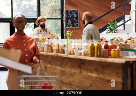 Femme noire regarde autour dans le magasin tout en tenant le panier rempli de produits alimentaires. L'accent sur le fond sont deux hommes, l'un un agriculteur avec des boîtes et l'autre un ouvrier de magasin, interagissant l'un avec l'autre. Banque D'Images