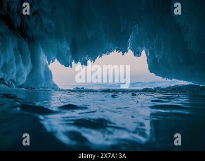 À l'intérieur d'une magnifique grotte de glace sur le lac Baïkal, de grands glaçons pendent du plafond, créant un paysage hivernal à couper le souffle. Les montagnes enneigées peuvent Banque D'Images
