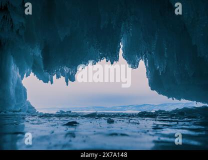 À l'intérieur d'une magnifique grotte de glace sur le lac Baïkal, de grands glaçons pendent du plafond, créant un paysage hivernal à couper le souffle. Les montagnes enneigées peuvent Banque D'Images