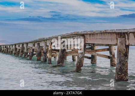 Photo d'une jetée en bois s'étendant dans la mer. Belle vue latérale sur la jetée. Eau de mer turquoise calme, structure de pont en bois et beau ciel. Banque D'Images