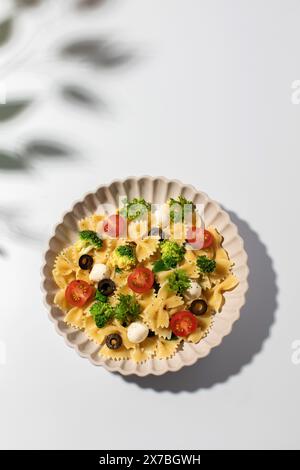 Salade de pâtes colorées avec farfalle, tomates cerises, olives, mozzarella, brocoli, et persil sur fond blanc Banque D'Images