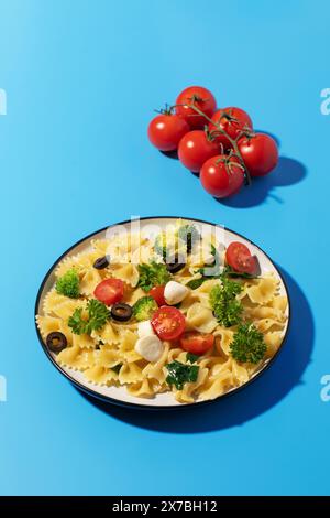 Délicieuse salade de pâtes avec farfalle, tomates cerises, olives, mozzarella, brocoli, et persil sur fond bleu. Banque D'Images