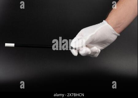 Main dans le gant blanc tenir la baguette magique isolé sur fond noir de studio Banque D'Images
