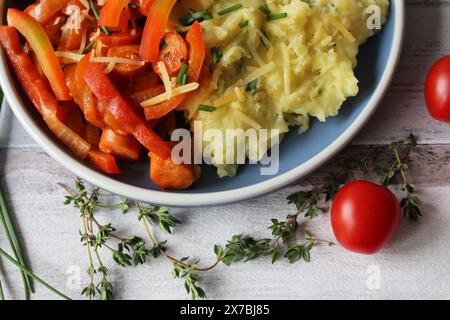 Ragoût de saucisse de pommes de terre au fromage avec des poivrons vibrants, des tomates et du thym frais Banque D'Images