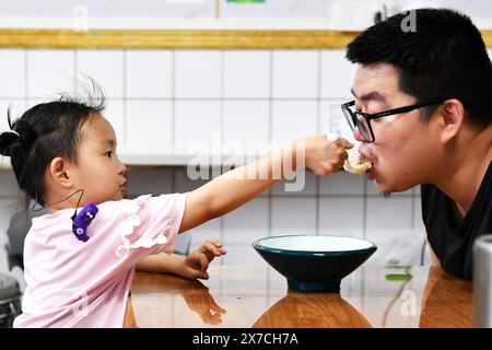 (240519) -- CHANGSHA, 19 mai 2024 (Xinhua) -- sa fille Zhang Yuhan interagit avec son père Zhang Yongsheng lors d'un souper à Changsha, dans la province du Hunan en Chine centrale, le 15 mai 2024. Bien que malentendants, Zhang Yongsheng et sa femme Zhan Jingwen ont réussi à faire entendre leur fille, qui souffre également du même handicap, à l'âge de deux ans. En tenant un stand de collation sur un marché nocturne et grâce au soutien de leurs proches et amis, le couple a réussi à se procurer un implant cochléaire pour l'oreille gauche de sa fille et une prothèse auditive pour l'oreille droite de celle-ci. « C'est trop cher pour h Banque D'Images