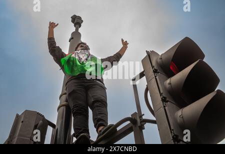 Londres, Royaume-Uni. 18 mai 2024 : un manifestant pro-palestinien arborant un drapeau palestinien se tient au-dessus d'un feu de circulation lors de la marche Nakba 76 pour la Palestine agai Banque D'Images