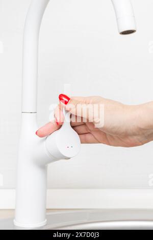 main femelle tourne le sélecteur sur le robinet de la cuisine. tournez la poignée du batteur à la main. la femme au foyer allume l'eau. robinet de cuisine blanc. photo verticale Banque D'Images
