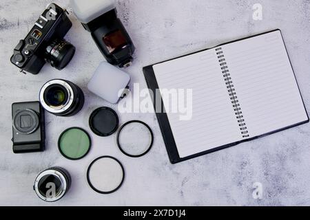 Cette image concerne un bloc-notes vierge, un appareil photo et des objectifs sur un fond blanc vue de dessus Banque D'Images