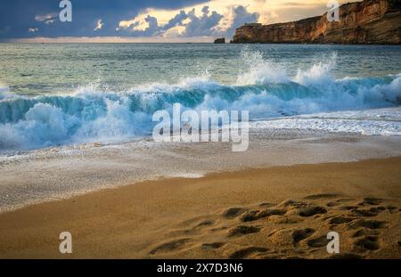 Empreintes de pas dans le sable devant les vagues qui s'écrasent à Nazare, au Portugal Banque D'Images