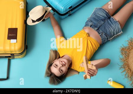 Belle jeune femme avec avion jouet, chapeau en osier, valises, passeport et bouteille de crème solaire couché sur fond bleu. Concept de voyage Banque D'Images