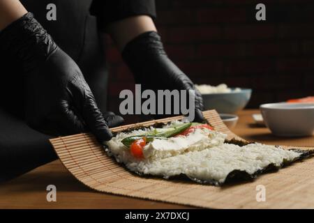 Chef en gants faisant rouler des sushis à la table en bois, gros plan Banque D'Images