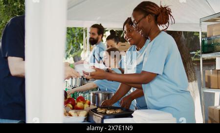 De généreux volontaires portant des t-shirts bleus donnent des repas gratuits et une aide humanitaire à ceux qui en ont besoin. Les pauvres et les sans-abri de toutes races sont nourris par l'organisation à but non lucratif. Vue latérale, portable. Banque D'Images