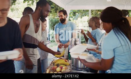 Des bénévoles distribuent gratuitement de la nourriture aux nécessiteux, faisant preuve de compassion et de soutien lors d'un événement de charité humanitaire. Bénévoles amicaux offrant des repas chauds et des aliments aux pauvres. Banque D'Images