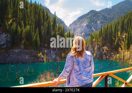 Femme regarde une forêt submergée dans le lac de montagne Kaindy au Kazakhstan. Vue panoramique sur le lac unique. Réserve naturelle. Banque D'Images