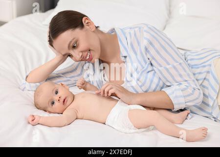 Jeune femme heureuse appliquant la crème pour le corps sur la peau du bébé sur le lit Banque D'Images