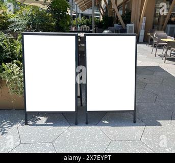 Maquette du panneau d'affiche verticale blanche blanche de publicité extérieure de ville sur le trottoir d'entrée du restaurant. Banque D'Images