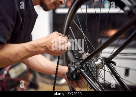 Réparateur travaillant : homme hispanique mettant la chaîne sur un vélo dans son atelier de vélo. De vraies personnes au travail. Banque D'Images