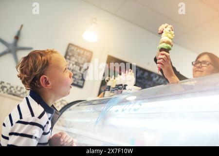 Crème glacée, heureux et enfant en magasin pour le dessert avec travailleur servant le dessert pour une friandise sucrée. Excité, envie et serveur avec une cuillère de gelato congelé Banque D'Images