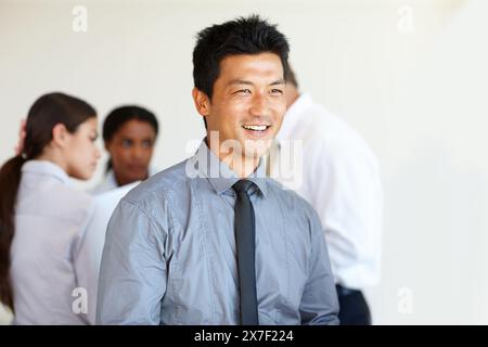 Homme d'affaires, sourire et penser au bureau avec team building et professionnels au travail. Asiatique, personne masculine et employés avec joyeux, heureux et Banque D'Images