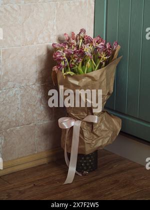 Gros plan vertical d'un bouquet de tulipes roses fanées dans un vase sur le sol dans le coin cuisine. Banque D'Images