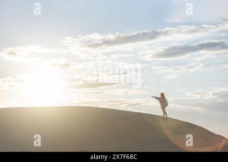 femme dans le désert marchant parmi les dunes au coucher du soleil contre le ciel, copiez l'espace dans le ciel Banque D'Images