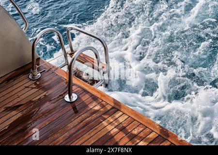 Pont arrière en bois de teck et échelle métallique d'un yacht à moteur, vagues et éclaboussures de mer et mousse. Banque D'Images