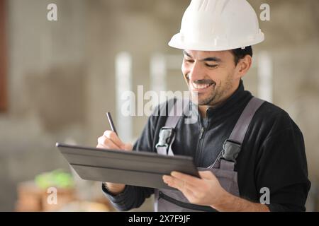 Heureux travailleur de la construction utilisant la tablette dans une maison Banque D'Images