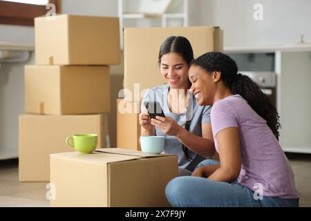 Des femmes noires et blanches vérifiant le téléphone déménageant la maison dans la cuisine Banque D'Images