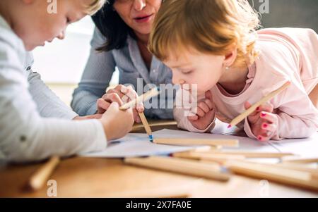 Grand-mère prend soin des petits-enfants pendant que leurs parents sont au travail, faisant de l'artisanat, dessinant sur du papier sur le sol. Banque D'Images