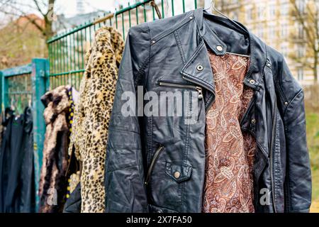 Vestes vintage sur une clôture : manteaux en cuir et imprimé léopard suspendus à l'extérieur dans un marché aux puces Banque D'Images