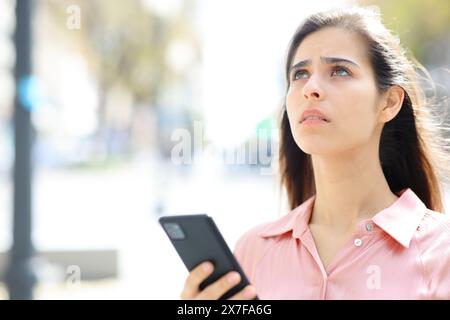 Femme inquiète tenant le téléphone regardant dans la rue Banque D'Images