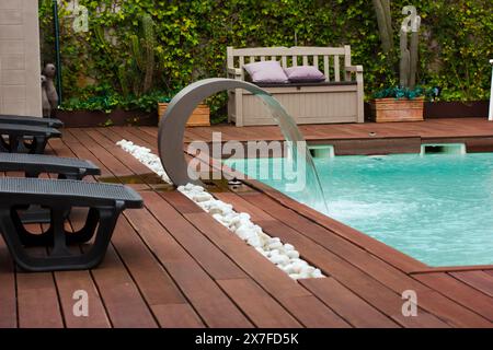 Chaises longues et piscine. Ruisseau cascade à l'infini dans un hôtel de luxe. Vacances estivales en station. Plancher en bois près de la piscine avec eau bleue. Banque D'Images