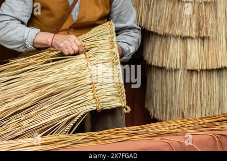 mains d'un artisan tissant une cape imperméable traditionnelle avec de la paille. Banque D'Images