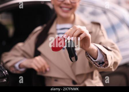 Femme tenant la clé à bascule de voiture près de son véhicule à l'extérieur, gros plan Banque D'Images