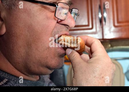 Vue de profil d'un homme portant des lunettes mangeant un hamburger. Banque D'Images