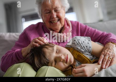 Fille endormie couchée la tête sur les genoux de la mère diplômée. Portrait d'une femme âgée passant du temps avec sa petite-fille. Banque D'Images