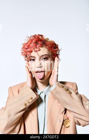 Une femme vibrante aux cheveux rouges dans une tenue colorée sort ludique sa langue. Banque D'Images