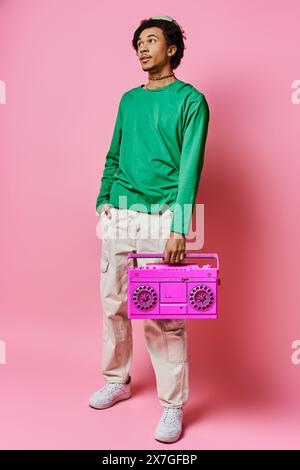 Un jeune homme afro-américain joyeux tenant une boombox rose devant un fond rose éclatant. Banque D'Images